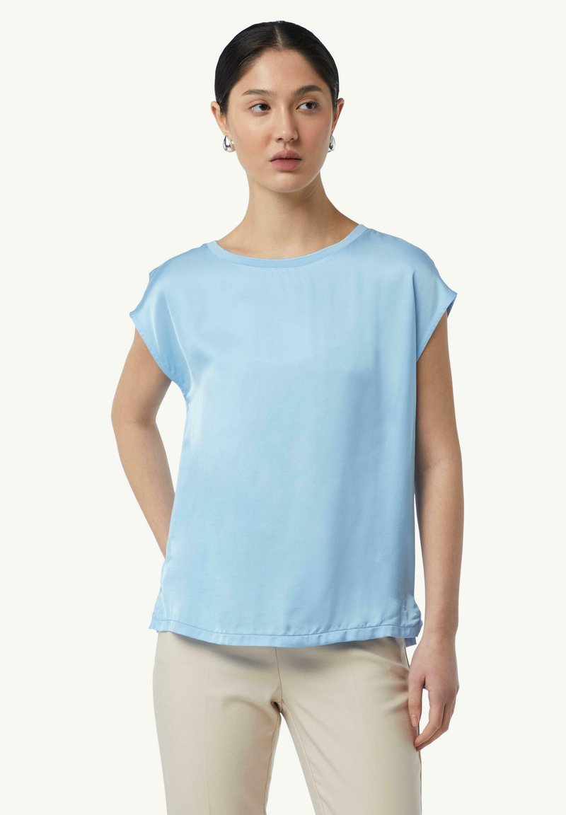 Jasnoniebieska bluzka krótki rękaw, wykonana z gładkiego materiału, z okrągłym dekoltem i luźnym krojem, która pasuje do beżowych spodni.