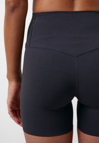 Mustat joustavat shortsit, joissa on korkea vyötärö, sileä pinta ja hienovaraiset ompelukoristeet, istuvat hyvin vartalolle.