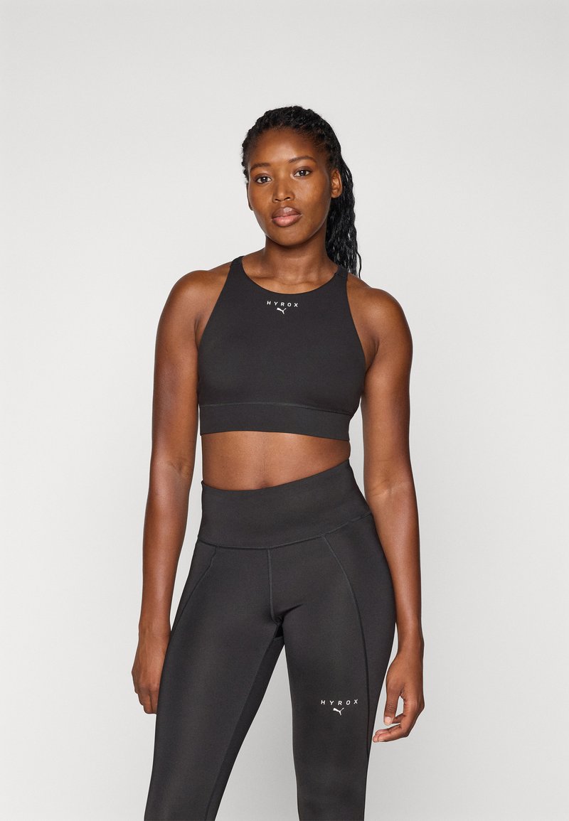 Top cropped atlético preto com um design ajustado e logótipo HYROX. Combinado com leggings pretas de cintura alta com costura contrastante e logótipo.