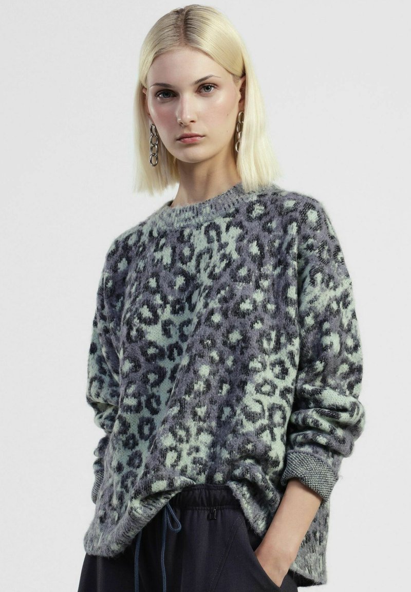 Maglione animalier in morbido materiale peloso; tonalità verde menta e grigio; vestibilità comoda con scollatura e polsini a coste, abbinato a pantaloni scuri.