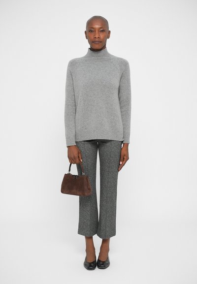 Grå turtleneck sweater, struktureret. Grå flagrende bukser med et spraglet mønster. Lille brunt suedetaske med en sølvlås. Sorte flade sko.