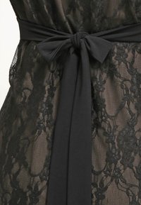 Robe en dentelle noire avec une superposition légère et un motif floral, dotée d'une ceinture en tissu noir uni nouée à la taille.