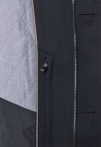 Černá a šedá zateplená bunda s prošívanou strukturou, vybavená zipovým zapínáním a boční kapsou s brandovaným zipem.