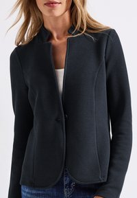 Blazer bleu marine foncé avec un tissage texturé, ouverture frontale, col mao et fermeture à un bouton. Coupe slim avec coutures discrètes.