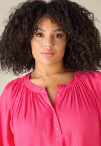 Ljust rosa skjorta med avslappnad passform, med knäppning fram och rynkade detaljer runt halsringningen. Slät tygtextur.