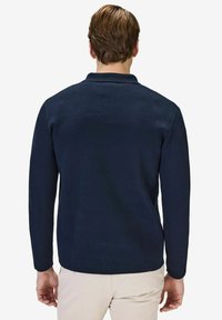 Marinblå långärmad polo med krage, tillverkad av textil med struktur. Bakview visar en ren design utan synliga mönster eller logotyper.