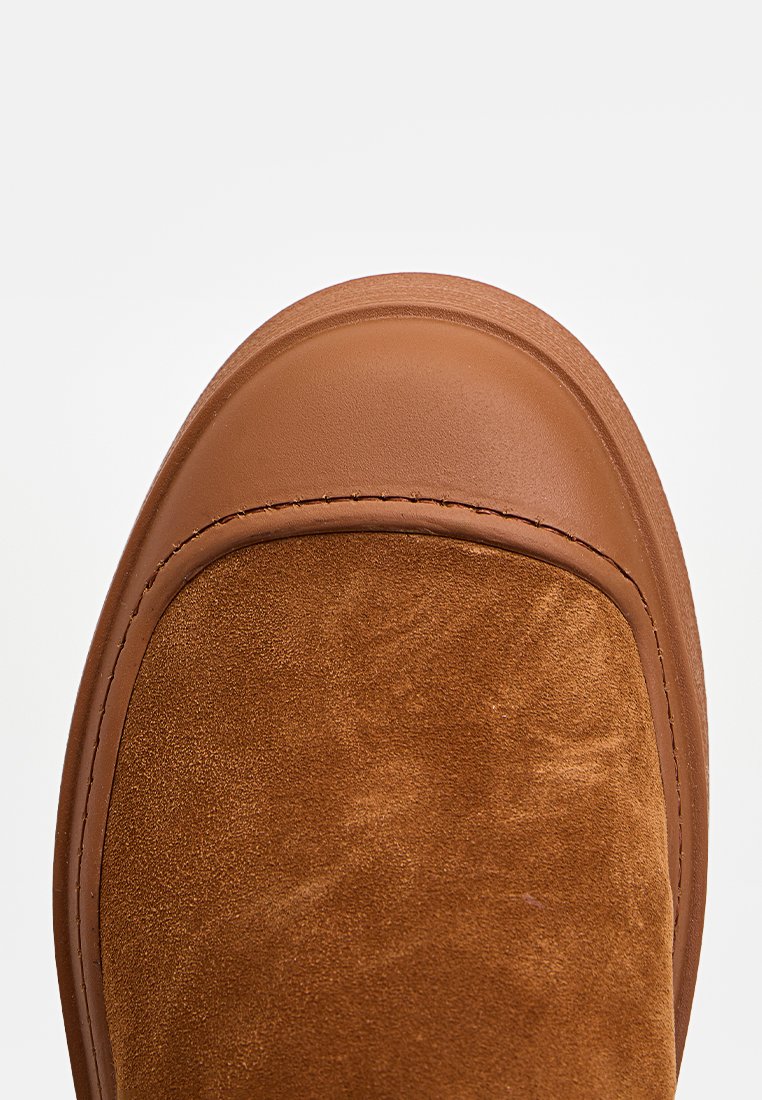 Braunes Wildleder-Schlupfschuh mit runder Zehenform. Verfügt über eine glatte Lederspitze und kontrastierendes Garn entlang der Kanten.