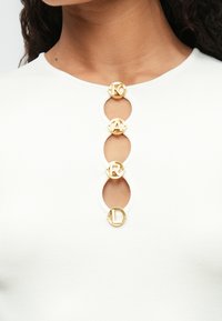 Biała top z prążkowanej tkaniny z falbaniastym dekoltem, ozdobiona czterema okrągłymi złotymi guzikami z literami K, A, R, L.