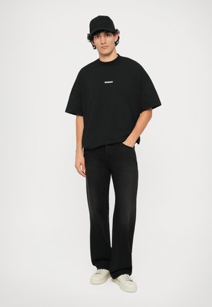 Czarny bawełniany oversized t-shirt z nadrukiem "BONSAI", zestawiony z czarnymi dżinsami i białymi sneakersami. W zestawie czarna czapka z ozdobą "VOLTAIRE".