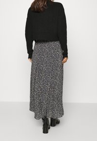 Suéter negro corto combinado con una falda maxi floral en azul oscuro, con patrones de flores en blanco y tonos pastel. Tejido de punto texturizado con mangas largas.