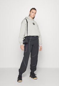 Sudadera gris claro con bolsillo frontal y logo; pantalones negros de tiro bajo con costuras azules; zapatillas negras; pequeño bolso cruzado negro.