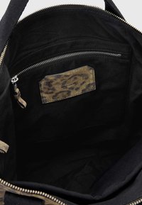 Interno di una borsa tote nera in tela con una tasca con zip e un pannello decorativo con stampa leopardata. Texture liscia con dettagli di cucitura robusti.