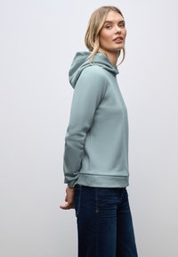 Felpa blu chiaro in pile con tasca a marsupio frontale, polsini e orlo a costine. Indossata con jeans blu scuro. Design semplice e minimal.
