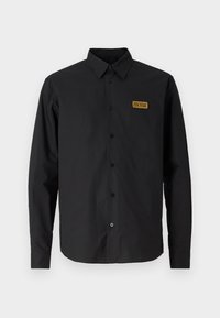 Black long-sleeve button-up shirt made of smooth fabric, featuring a structured collar, a chest patch with logo, and black buttons.