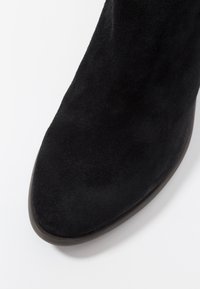 Mustat mokkanahkasaappaat nilkkapituiset, joissa on tyylikäs muotoilu, teräväkärkinen malli ja sileä pinta. Pohja on kontrastiväristä tummaa materiaalia.