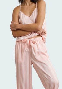 Pijamas de satén rosa claro con un patrón a rayas. La parte superior tiene tirantes finos y un escote en V, mientras que los pantalones cuentan con una cintura ajustable con cordón.