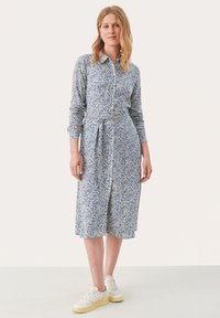 Abito midi blu a fiori con maniche lunghe, chiusura frontale a bottoni e cintura in tessuto. Abbinato a sneakers bianche con suola texturizzata.