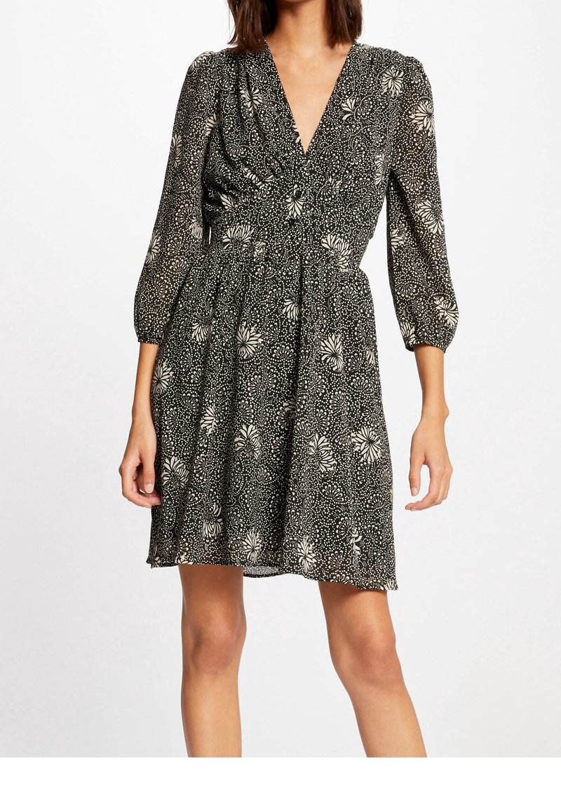 Black dress with white floral pattern, v-neck, and gathered waist. Features three-quarter sleeves and a flared skirt with light texture.