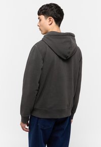 Sudadera con capucha de color gris oscuro, de corte relajado, con puños y dobladillo acanalados, que presenta una textura suave. Combinada con pantalones de mezclilla azul.