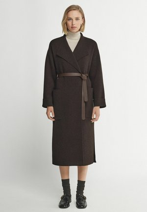 Mørkebrun uldomslagjakke med en bred krave, lange ærmer, to frontlommer og et matchende bælte. Tekstureret stof og ankellang design.