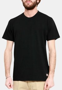 Maglietta nera in cotone con maniche corte, collo a giro e taglio dritto; presenta un piccolo badge con logo sul lato sinistro in basso.