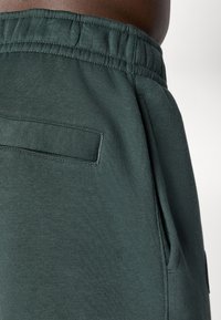 Grønne bomullssweatpants med elastisk midje, side- og baklommer, og en glatt tekstur. Har en subtil, ensfarget finish.