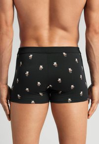 Boxer ajustados negros hechos de una tela suave con un patrón repetido de pequeños osos de dibujos animados en varios colores. Estilo con un corte ajustado.
