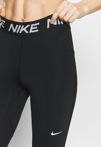 Czarne legginsy wykonane z elastycznej tkaniny z szerokim pasem w talii, na którym znajduje się białe logo Nike. Na nodze dodatkowo znajduje się mały biały swoosh Nike.