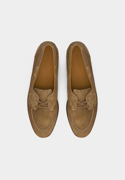 Ζευγάρι καφέ μοκασίνια από σουέντ με κορδόνια, στρογγυλεμένες μύτες και εμφανή ραφή, σε θέα από πάνω πάνω σε απλό φόντο.