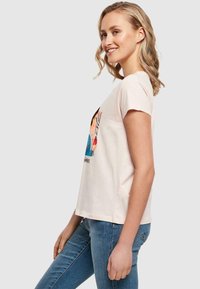Lyse rosa bomull T-skjorte med korte ermer, med et fargerikt grafisk design på forsiden. Rett kutt nederst, brukt med blå jeans.
