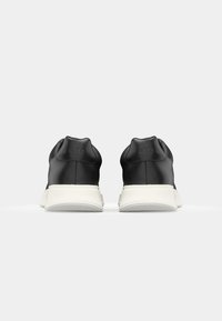 Schwarze synthetische Sneaker mit strukturiertem Obermaterial, weißer Gummisohle, gepolstertem Kragen und geprägtem Branding an der Ferse.