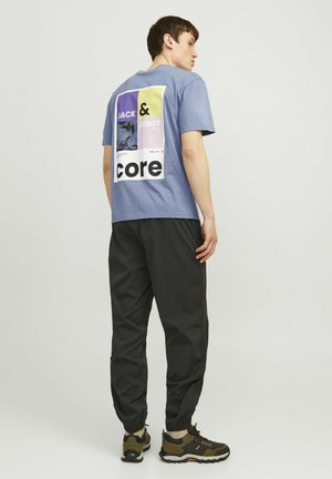Tricou din bumbac albastru cu imprimeu grafic pe spate, asortat cu pantaloni joggers negri și adidași negri. Are guler rotund și mânecă scurtă.