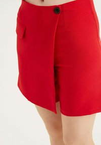 Pantaloni corti rossi in tessuto liscio, caratterizzati da una chiusura con bottone laterale e una tasca singola, con orlo pulito e vestibilità su misura.