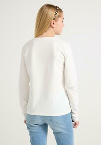 Hvid langærmet skjorte med rund halsudskæring og glat tekstur, parret med lyseblå jeans. Har tætsiddende ærmer og en afslappet pasform.