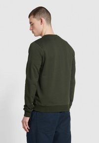 Sweatshirt vert olive à manches longues, avec des poignets et un ourlet côtelés, un col rond et une texture lisse, porté avec un pantalon bleu marine.