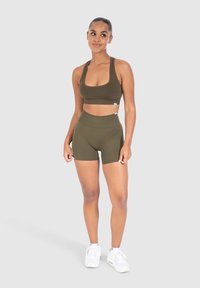 Olijfgroen sport-bh en set van hoge taille shorts, gemaakt van rekbaar materiaal met een gladde textuur. Witte sneakers maken de outfit compleet.