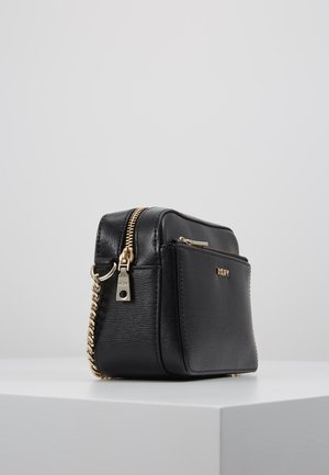 Musta nahkainen crossbody-laukku, jossa etutasku vetoketjulla, kultainen vetoketju, ketjuhihna ja DKNY-logo taskussa, esitetty valkoisella pinnalla.
