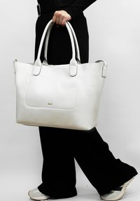 Witte leren tote bag met een gestructureerde afwerking, dubbele handgrepen en een gladde voorzak. Minimalistisch ontwerp met een metallic logo-accent.