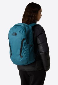 Turkosfärgad North Face Vault-ryggsäck med vadderade axelremmar, meshnätfickor på sidan, logotypdetalj och en elegant rektangulär design.