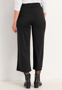 Zwarte cropped broeken met een brede pijp en een elastische tailleband. Gekocht met zwarte enkellaarzen met een chunky hak. Gladde textuur.