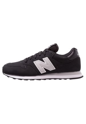 Schwarzer New Balance Sneaker mit weißem Logo, schwarzen Schnürsenkeln und weißer Sohle von der Seite vor weißem Hintergrund.