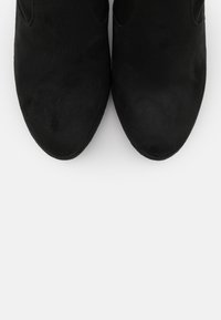 Svarta mockaskor ankla med en slät yta, spetsig tå, urklippta sidor och en elegant, minimalistisk design.