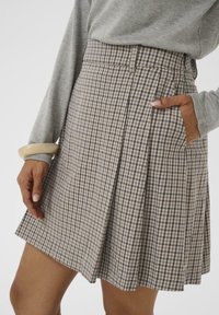 Karierte Röcke in Beige und Marineblau, mit Falten und seitlichen Taschen. Hergestellt aus einem strukturierten Stoff, entworfen mit einem Bund und lockerer Passform.