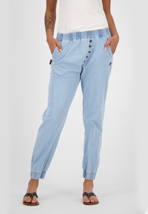Personne portant un pantalon jogger bleu clair à taille élastique avec boutons et poches, associé à des sandales noires et un haut blanc.