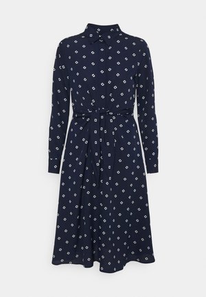Robe-chemise bleu marine à manches longues avec motif losanges blancs, col, boutonnage sur le devant, et ceinture assortie en tissu à la taille.