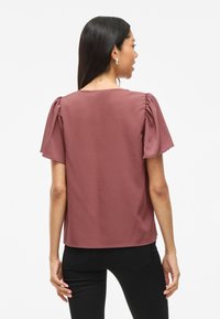 Blusa borgogna con maniche corte a palloncino e vestibilità rilassata. Realizzata in tessuto morbido, presenta un design semplice senza fantasie.
