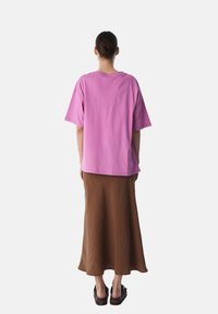 T-shirt in cotone oversize rosa abbinato a una gonna midi marrone. La t-shirt ha maniche corte e un colletto rotondo; la gonna è fluida con una texture liscia.