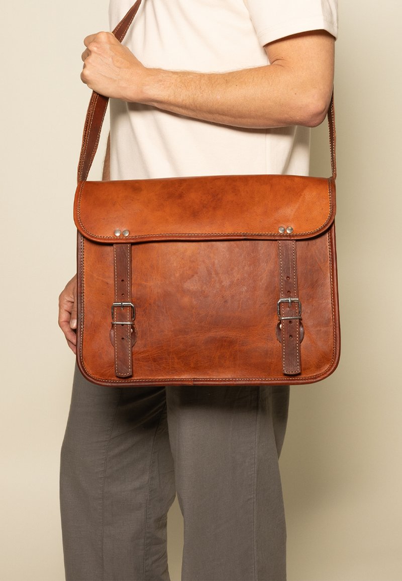 Bruine leren schoudertas met een grote klep, twee verstelbare gespen en een schouderband. Gladde textuur en minimale metalen accenten.