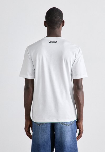 White cotton t-shirt with short sleeves, featuring a black 'MOSCHINO' logo on the back neck. Worn with light blue denim shorts.