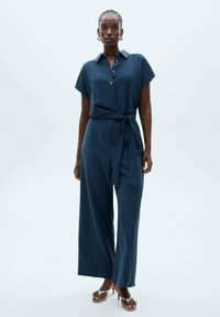 Tuta blu navy con maniche corte, colletto con bottoni e vita cinturata; presenta pantaloni a gamba larga e una texture liscia.